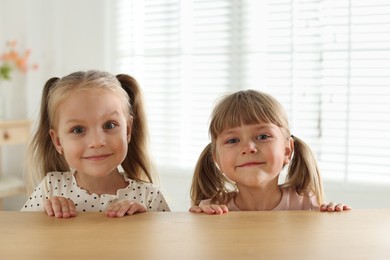 Photo of Curious little girls peeking over wooden table indoors