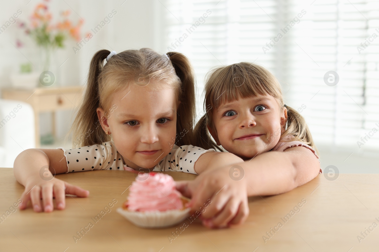 Photo of Cute little girls reaching for tasty dessert at wooden table indoors