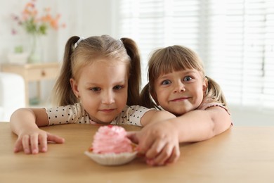 Photo of Cute little girls reaching for tasty dessert at wooden table indoors