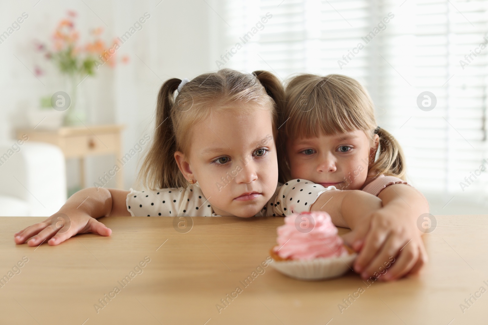 Photo of Cute little girls reaching for tasty dessert at wooden table indoors