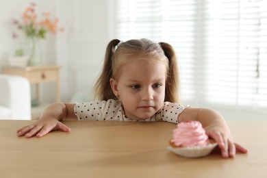 Photo of Cute little girl reaching for tasty dessert at wooden table indoors