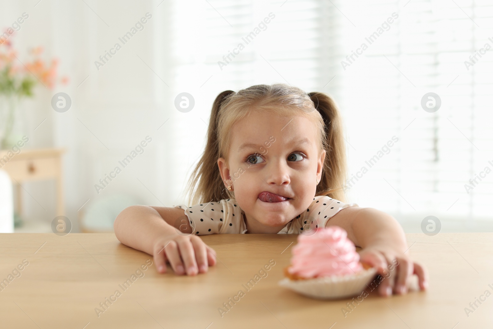 Photo of Cute little girl reaching for tasty dessert at wooden table indoors