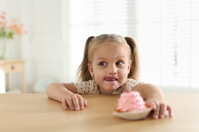 Photo of Cute little girl reaching for tasty dessert at wooden table indoors