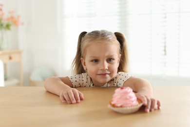 Photo of Cute little girl reaching for tasty dessert at wooden table indoors