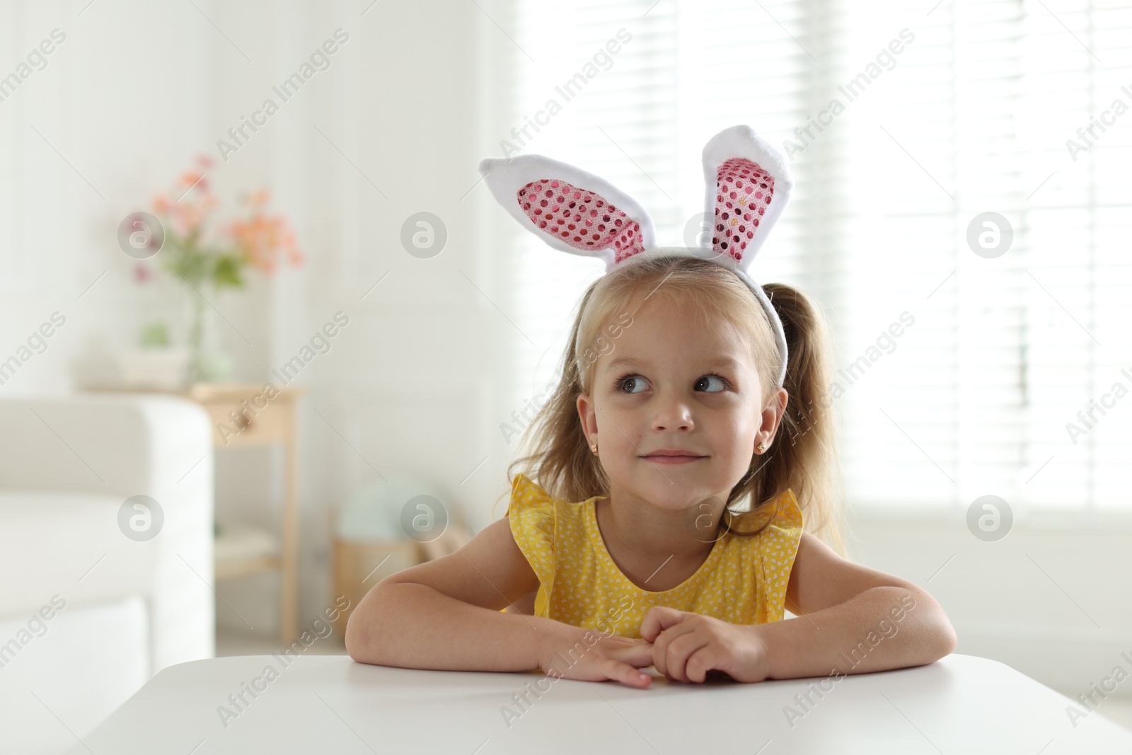 Curious little girl in bunny ears at white table indoors Photo of Curious little girl in bunny ears at white table indoors