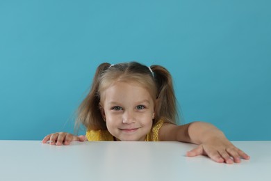 Photo of Curious little girl peeking over white table against light blue background