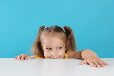 Photo of Curious little girl peeking over white table against light blue background