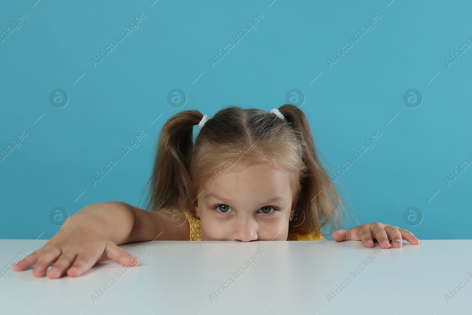 Photo of Curious little girl peeking over white table against light blue background