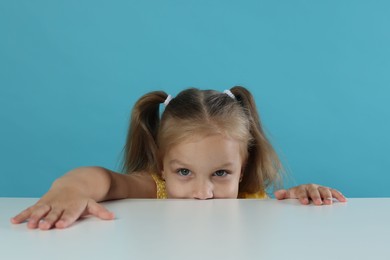 Photo of Curious little girl peeking over white table against light blue background
