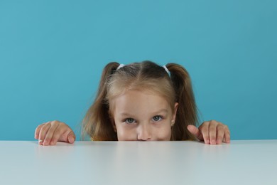 Photo of Curious little girl peeking over white table against light blue background
