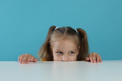 Photo of Curious little girl peeking over white table against light blue background