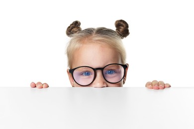 Photo of Curious little girl in glasses peeking over table against white background