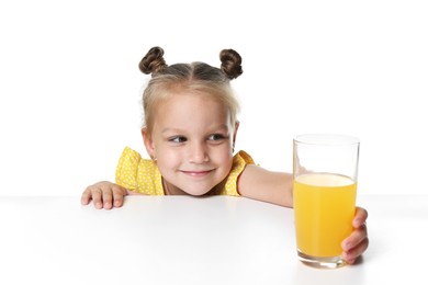 Photo of Cute little girl reaching for glass of orange juice at table against white background