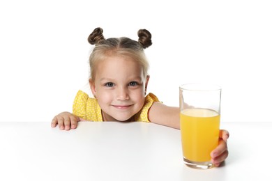Photo of Cute little girl reaching for glass of orange juice at table against white background