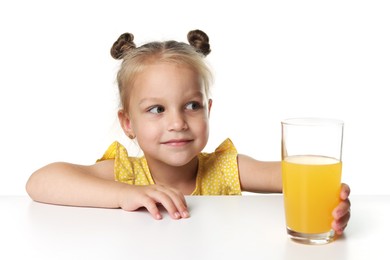Photo of Cute little girl reaching for glass of orange juice at table against white background