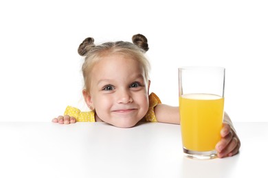 Photo of Cute little girl reaching for glass of orange juice at table against white background