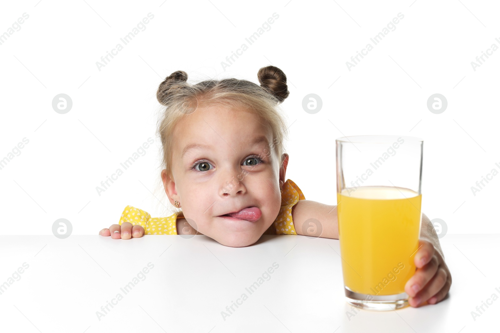 Cute little girl reaching for glass of orange juice at table against white background Photo of Cute little girl reaching for glass of orange juice at table against white background