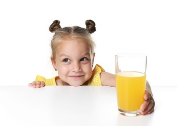 Photo of Cute little girl reaching for glass of orange juice at table against white background