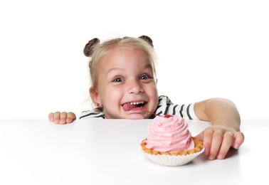 Photo of Cute little girl reaching for tasty dessert at table against white background
