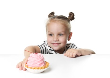 Photo of Cute little girl reaching for tasty dessert at table against white background