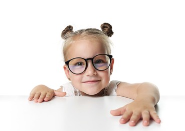 Photo of Curious little girl in glasses peeking over table against white background
