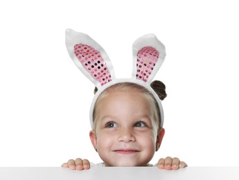 Photo of Curious little girl in bunny ears peeking over table against white background