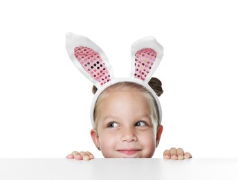 Photo of Curious little girl in bunny ears peeking over table against white background