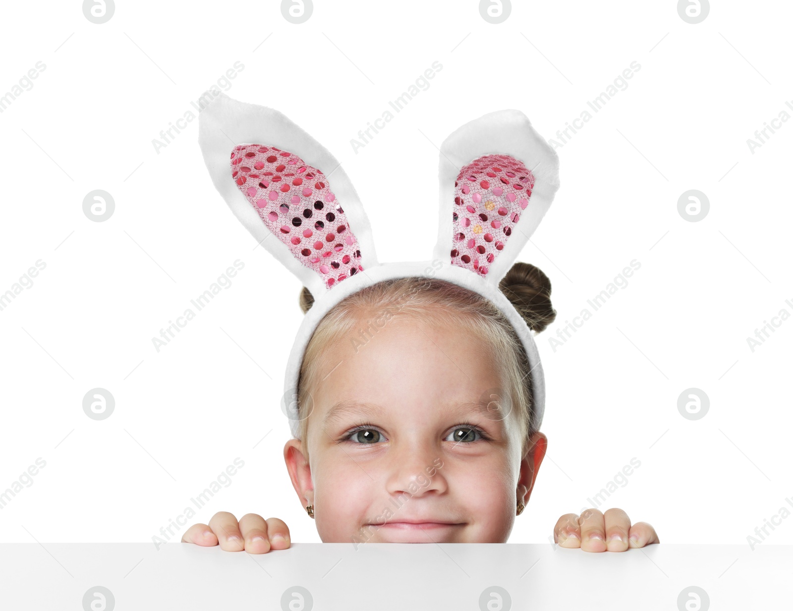 Photo of Curious little girl in bunny ears peeking over table against white background