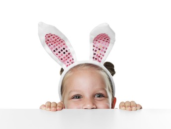 Photo of Curious little girl in bunny ears peeking over table against white background