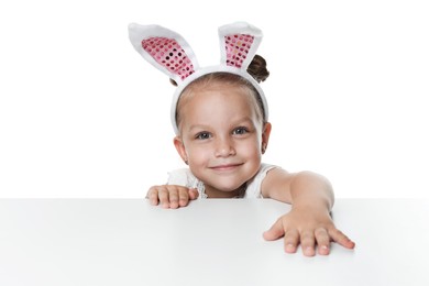 Photo of Curious little girl in bunny ears peeking over table against white background