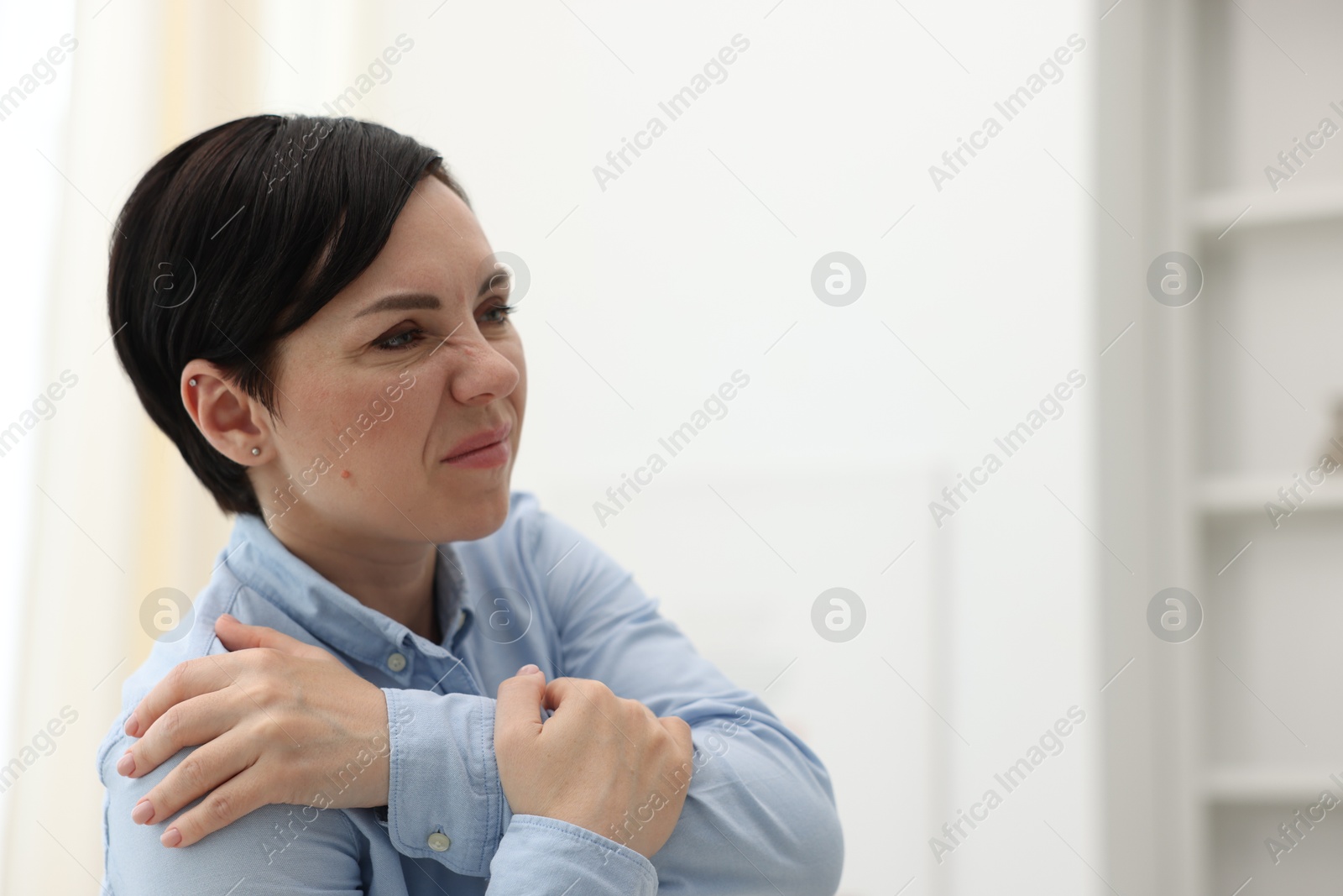 Photo of Woman suffering from shoulder pain at home. Space for text