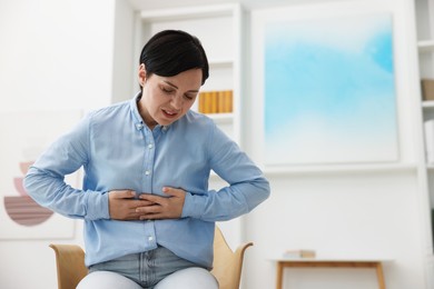 Photo of Woman suffering from stomachache at home. Space for text