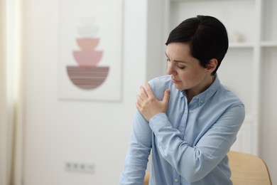 Photo of Woman suffering from shoulder pain at home. Space for text