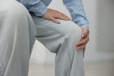Photo of Woman suffering from knee pain at home, closeup