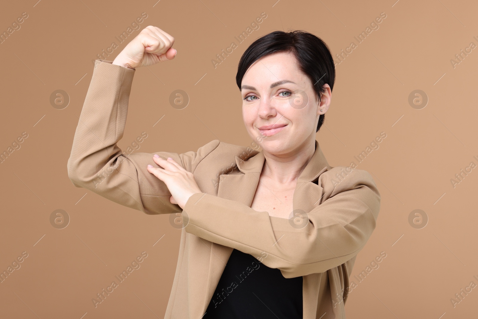 Photo of Strength. Beautiful businesswoman in suit showing her biceps on beige background