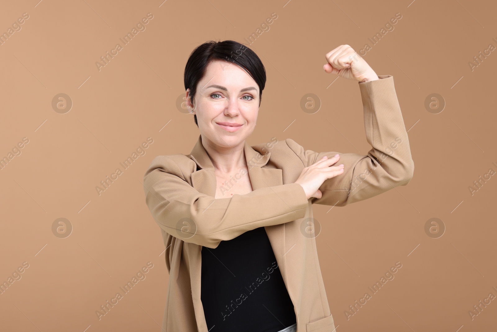 Photo of Strength. Beautiful businesswoman in suit showing her biceps on beige background