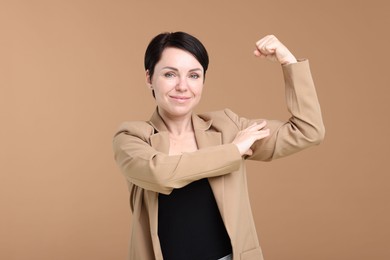 Photo of Strength. Beautiful businesswoman in suit showing her biceps on beige background