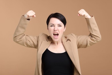 Photo of Strength. Emotional businesswoman in suit showing her biceps on beige background