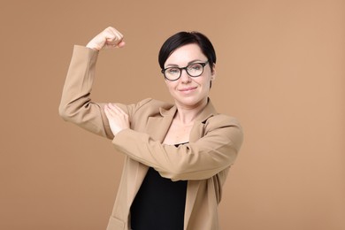 Photo of Strength. Beautiful businesswoman in glasses and suit showing her biceps on beige background