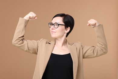 Photo of Strength. Beautiful businesswoman in glasses and suit showing her biceps on beige background