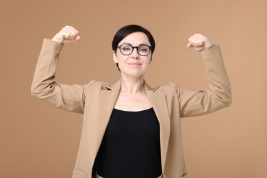 Photo of Strength. Beautiful businesswoman in glasses and suit showing her biceps on beige background
