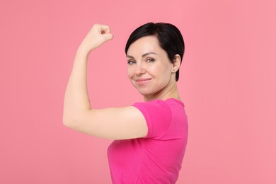 Photo of Strength. Beautiful woman showing her biceps on pink background