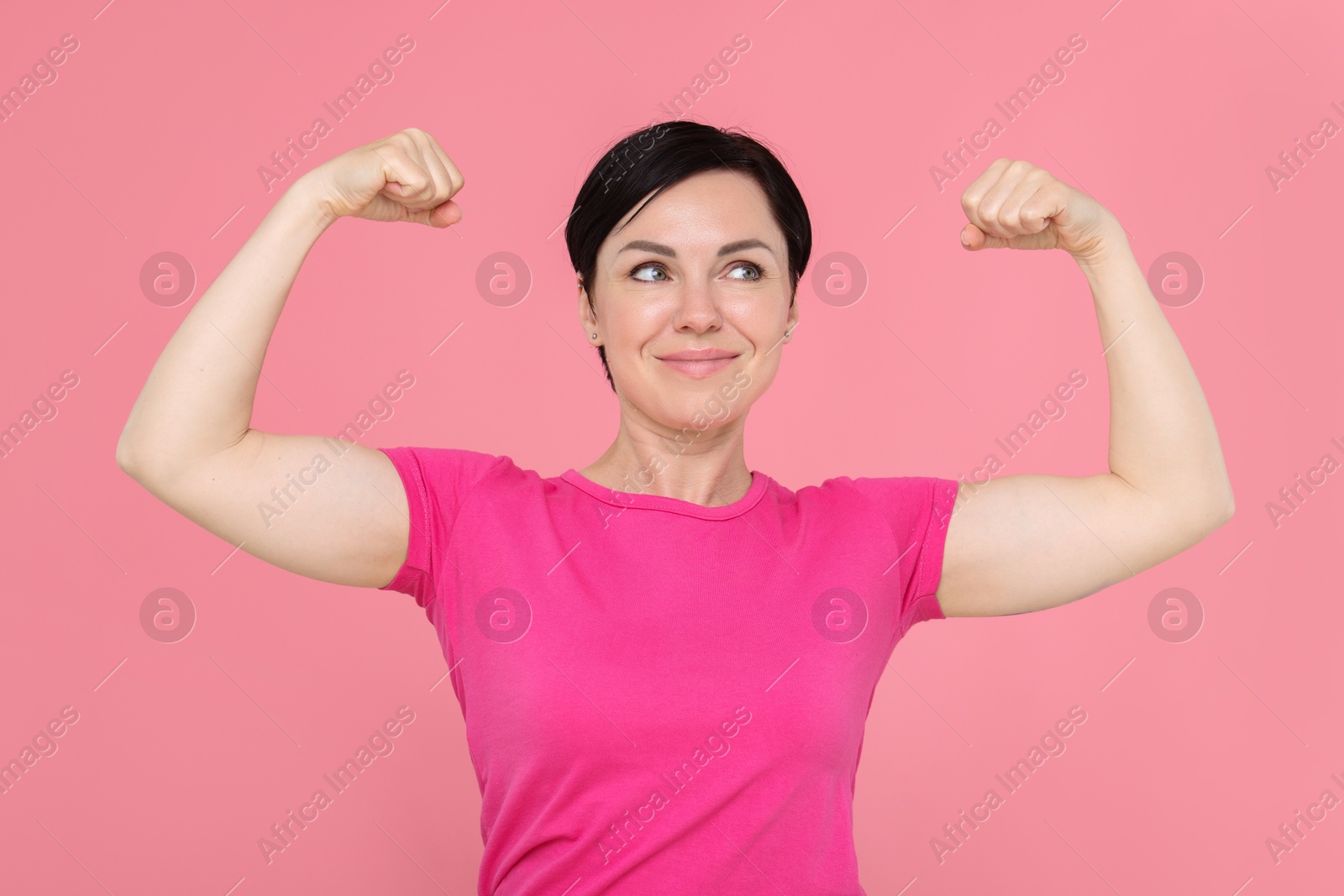Photo of Strength. Beautiful woman showing her biceps on pink background