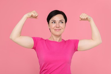 Photo of Strength. Beautiful woman showing her biceps on pink background