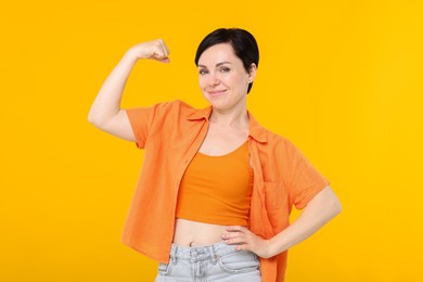 Photo of Strength. Beautiful woman showing her biceps on yellow background