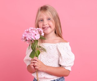 Photo of Portrait of smiling little girl with hydrangea flowers on pink background