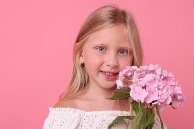 Photo of Portrait of smiling little girl with hydrangea flowers on pink background
