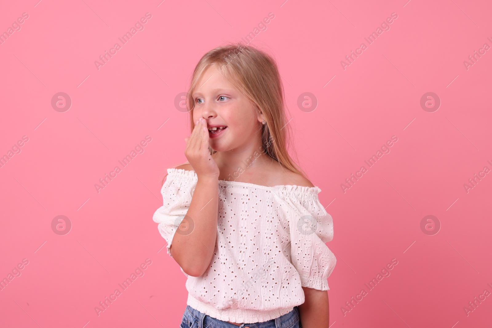 Photo of Cute little girl covering mouth and laughing on pink background