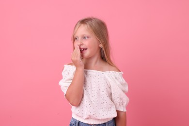 Photo of Cute little girl covering mouth and laughing on pink background