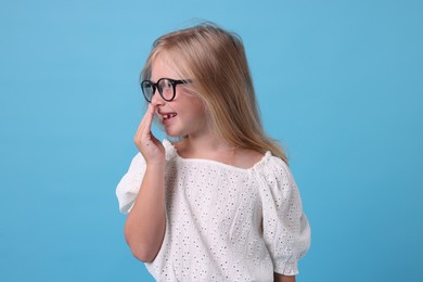 Photo of Cute little girl in glasses covering mouth and laughing on light blue background